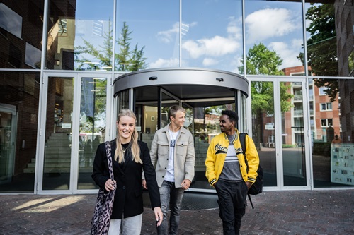 Drie studenten verlaten een schoolgebouw met een glazen gevel.