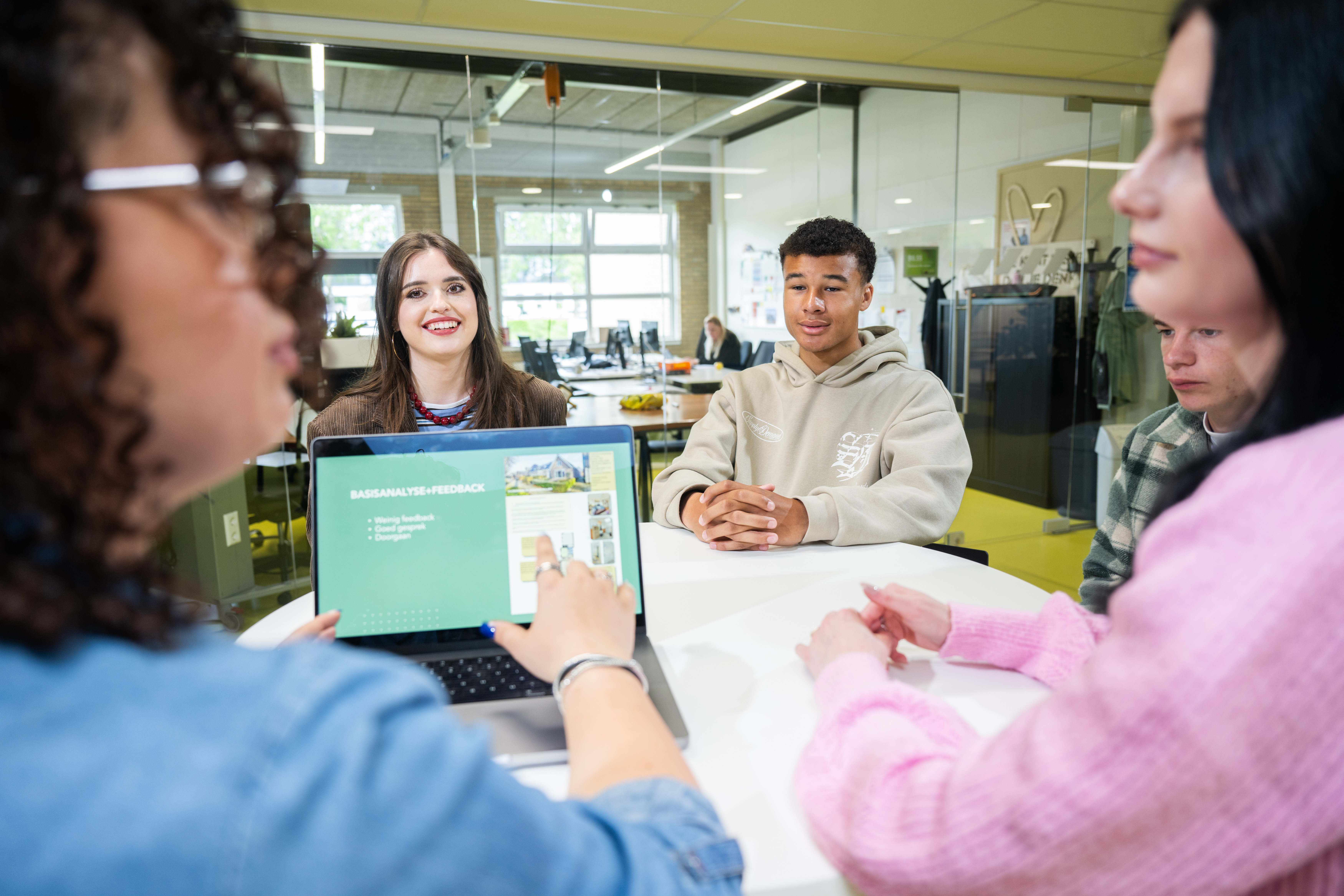 Studenten werken samen aan tafel met laptop in een leeromgeving.