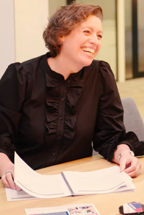 Docent lachend aan tafel met een notitieboek