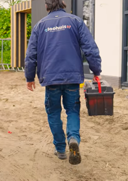 Student loopt weg met een zwarte gereedschapskist; draagt blauwe werkjas
