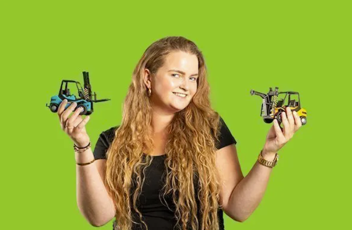 Student toont twee speelgoedheftrucks voor een groene achtergrond.